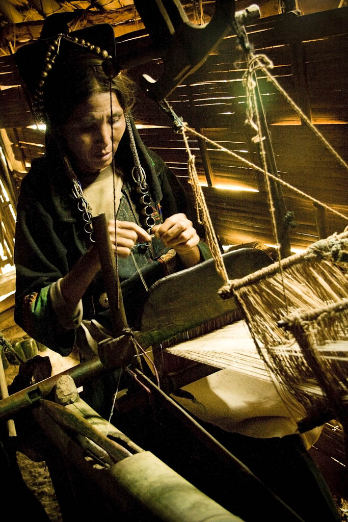 Woman spins the wood needle, she is weaving the cotton to produce the traditional akha indigo fabric. In these villages, women always wear the traditional clothes made from this fabric. Akha people. Mountains Between Phongsali and Chinese border. Laos.